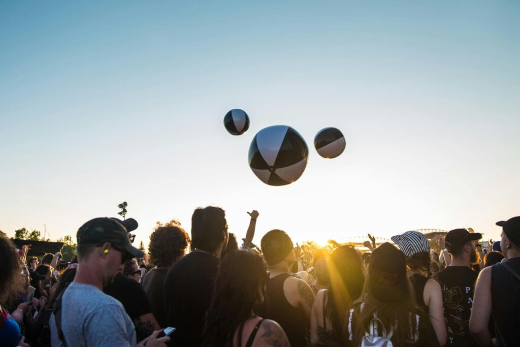 Group of people at a music festival standing as three beach balls are in the air.