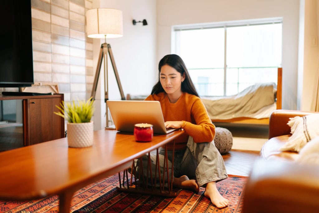 Girl sits on carpet, smiling at her laptop