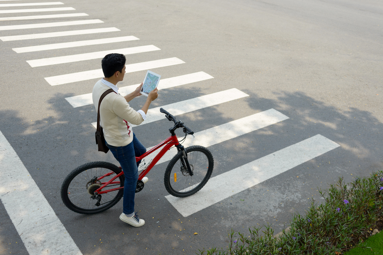 student-riding-a-bicycle-on-the-street-using-a-campus-map-on-his-tablet