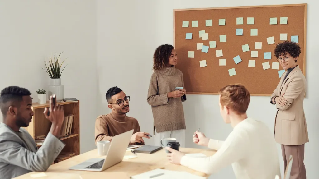 5 people working around a table putting ideas on sticky notes onto a board.