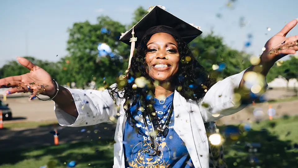 Woman with a graduation cap on throwing glitter at the camera.