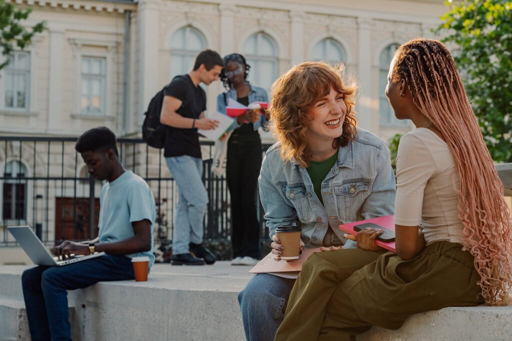 Two female students laugh at each other's jokes on a campus.